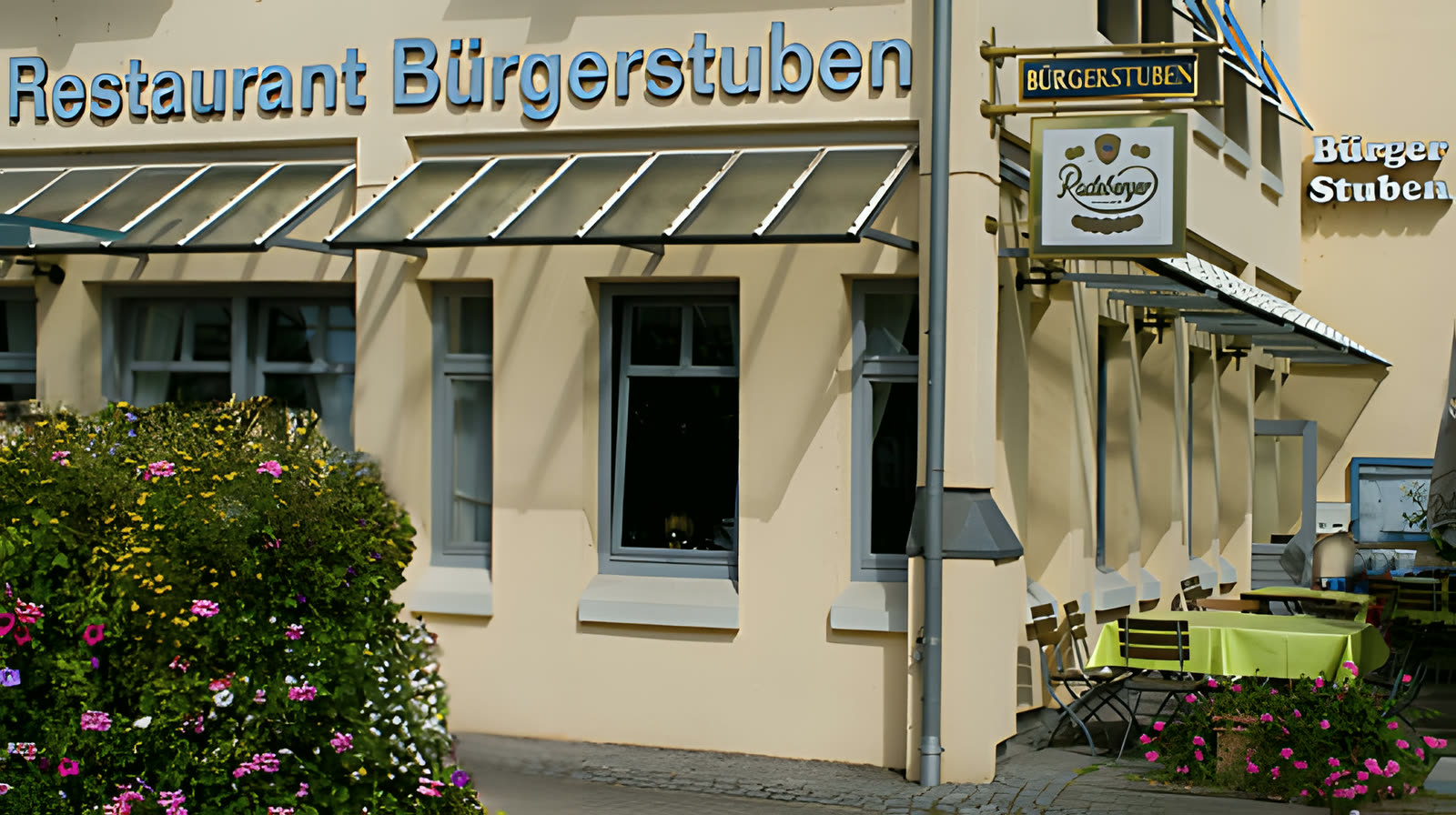 Außenansicht der Bürgerstuben Pleidelsheim mit cremefarbener Fassade, grünem Vordach und Bürgerstuben-Wappen
