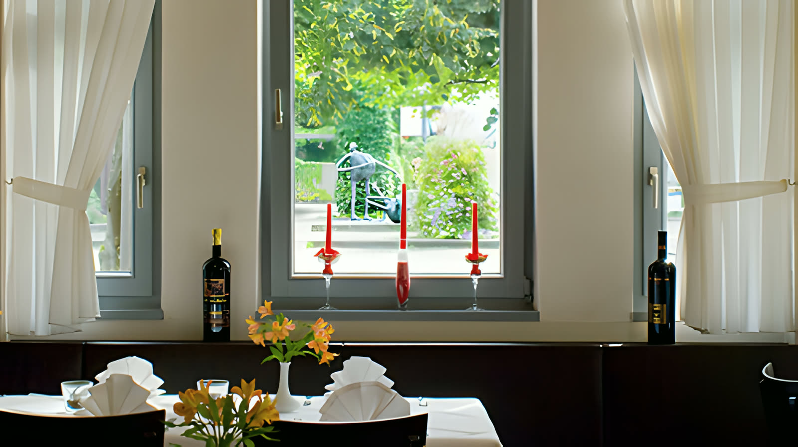 Fenster mit roten Kerzen, Rotweinflaschen und Blick in den Garten